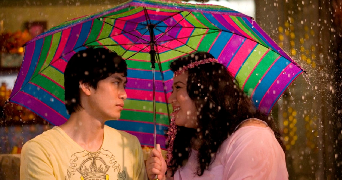 A couple shares a colorful umbrella in the rain, a romantic scene from the Singaporean film "12 Lotus".