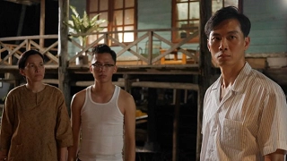 Three characters from the film "1965" stand in front of a wooden building, depicting a scene from Singapore's past.