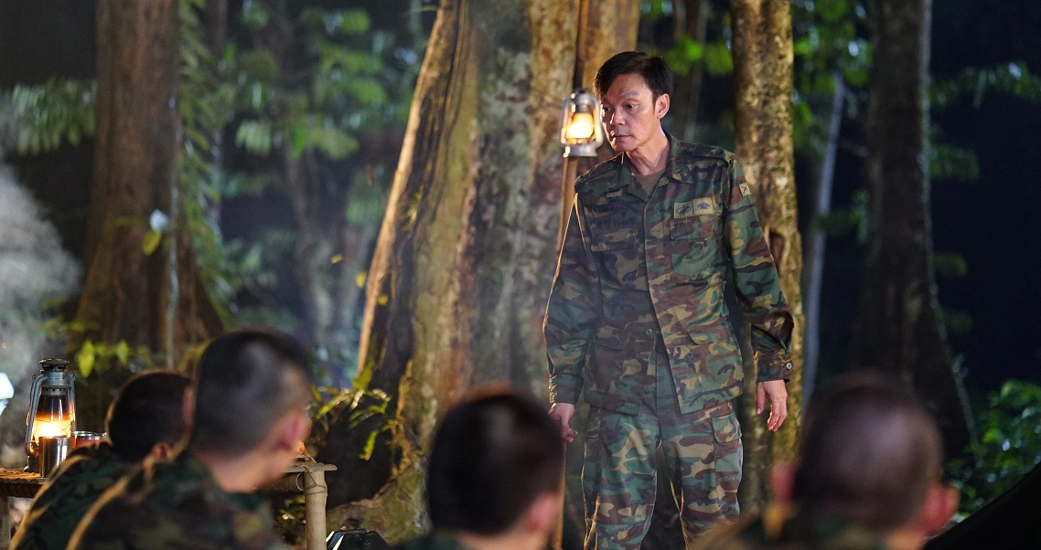 A soldier in camouflage uniform addresses a group in a dark forest setting, a tense scene from the horror film "2359 The Haunting Hour".