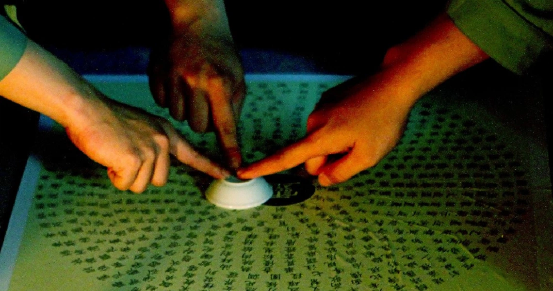 A film still from "2359" shows hands gathered around a circular object on a table with mysterious symbols, creating an eerie atmosphere.