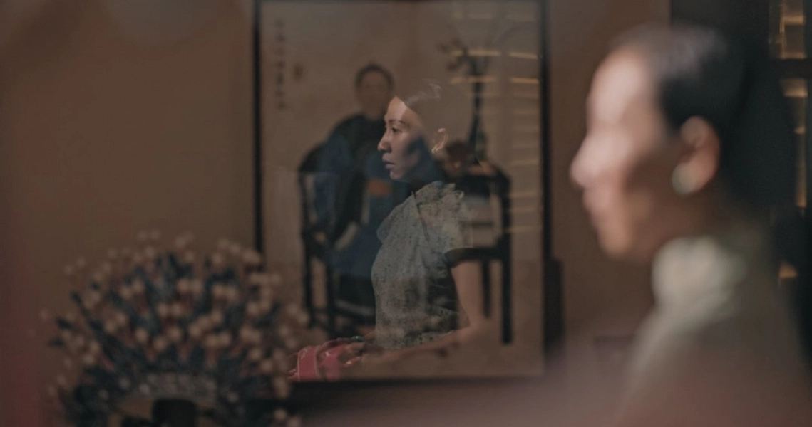 Film still from "667" showing a woman's reflection in a mirror, with another person's profile in the foreground.