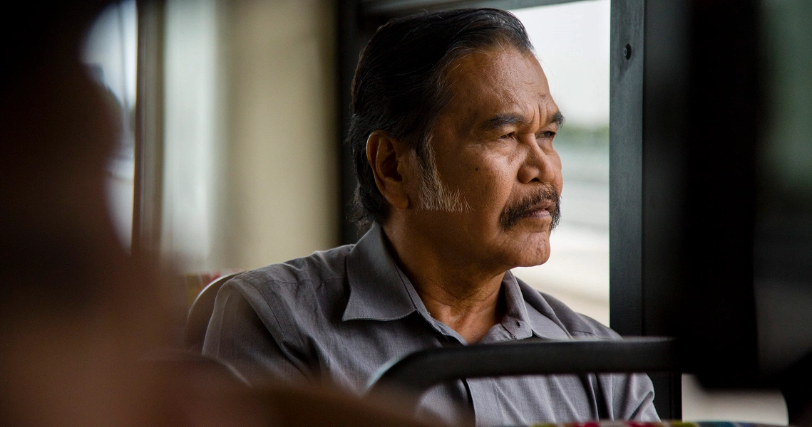 A pensive older man gazes out a window in a poignant scene from the Singaporean film "7 Letters".