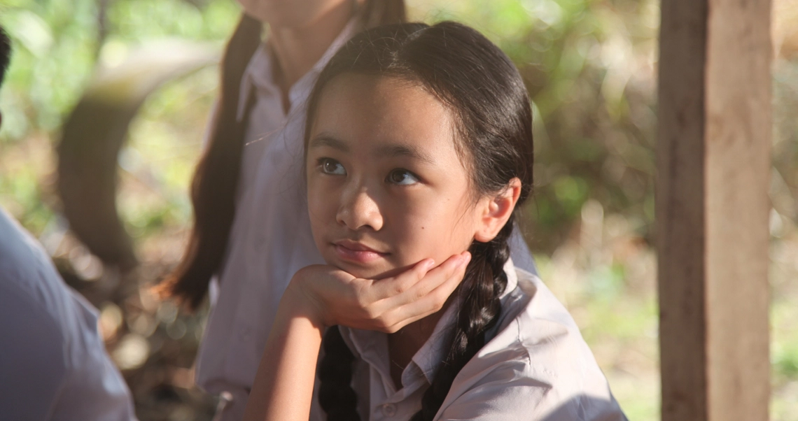 A young girl with braided hair smiles thoughtfully in a scene from the Singaporean film "7 Letters".