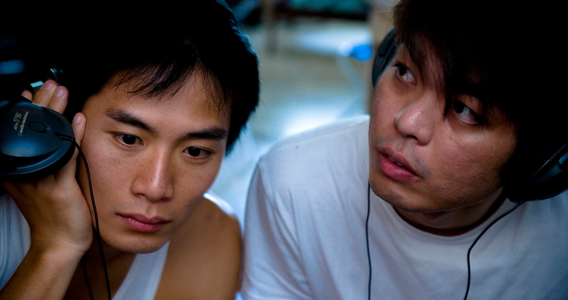 Two young men from the film 881 listen intently with headphones, showcasing a scene from the Singaporean musical drama.