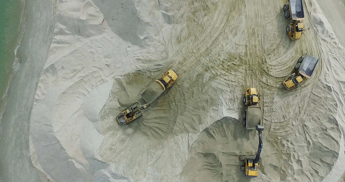 Aerial view of construction vehicles in a sandy landscape from "A Land Imagined" film still, showcasing industrial development.