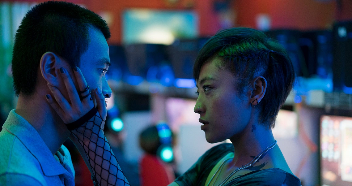 A dramatic scene from "A Land Imagined" shows two characters in intense conversation, bathed in neon blue and green lighting.