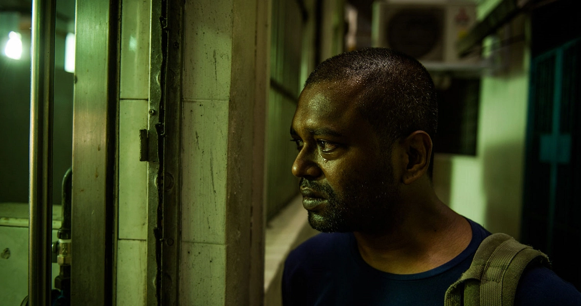 A dimly lit scene from the film "A Yellow Bird" showing a man with a serious expression in a shadowy, urban environment.