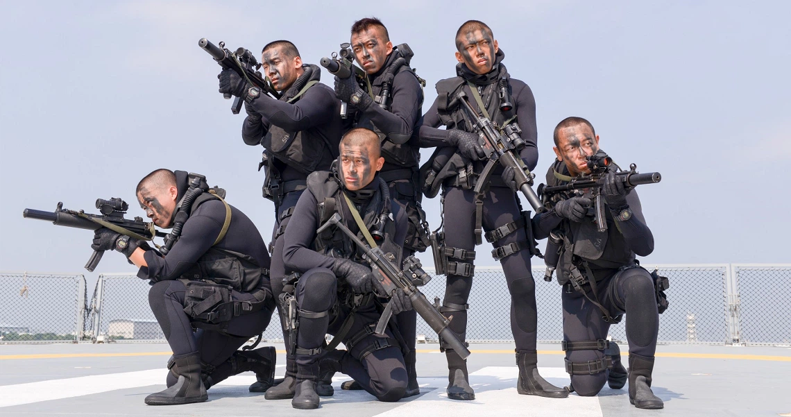 Armed soldiers in combat gear from the film "Ah Boys To Men 3 Frogmen" pose with weapons in a group formation.