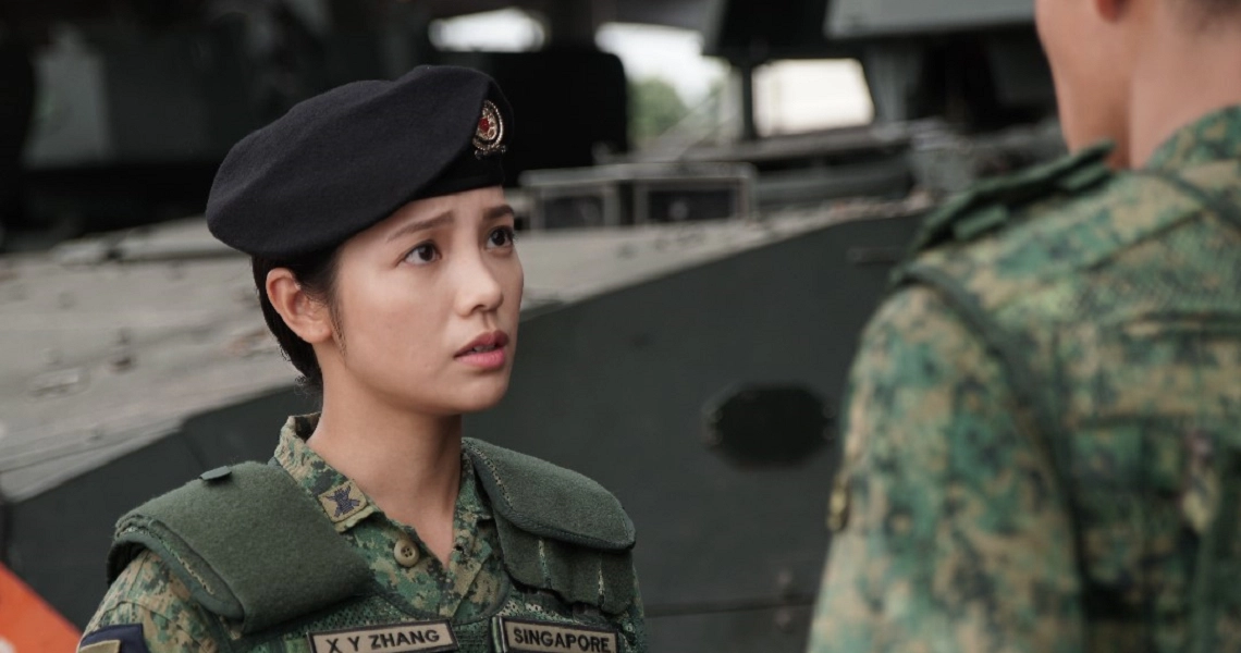 A female soldier in uniform and beret looks intently at another soldier in a scene from the film "Ah Boys To Men 4".