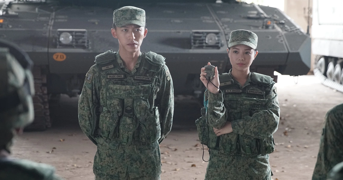 Two soldiers in green uniforms stand at attention in front of a military vehicle in a scene from the film Ah Boys To Men 4.