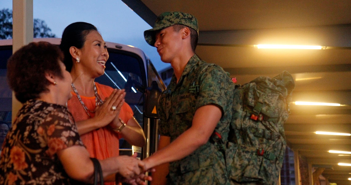 A soldier in uniform greets two smiling women in a scene from the Singaporean film "Ah Boys to Men".