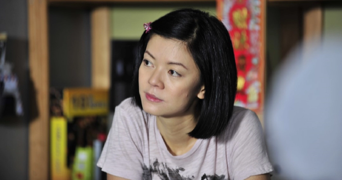 A woman with short black hair in a white shirt looks thoughtfully to the side in a film still from "Already Famous."