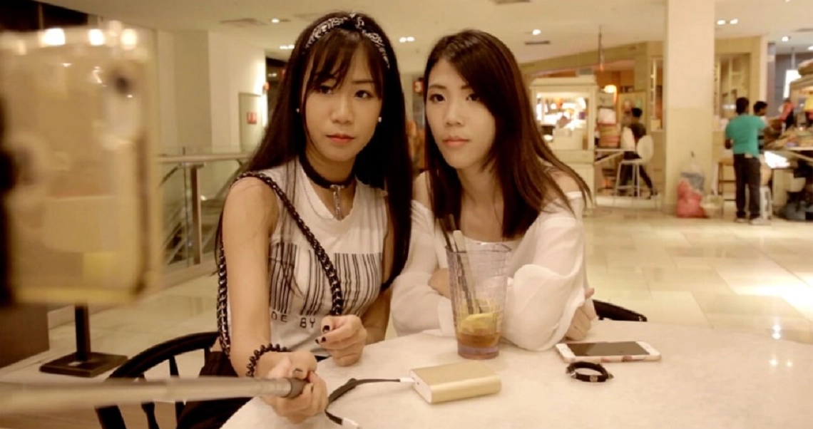 Two young women from the film "Ariel and Olivia" sit together at a table in a bright, modern cafe setting.