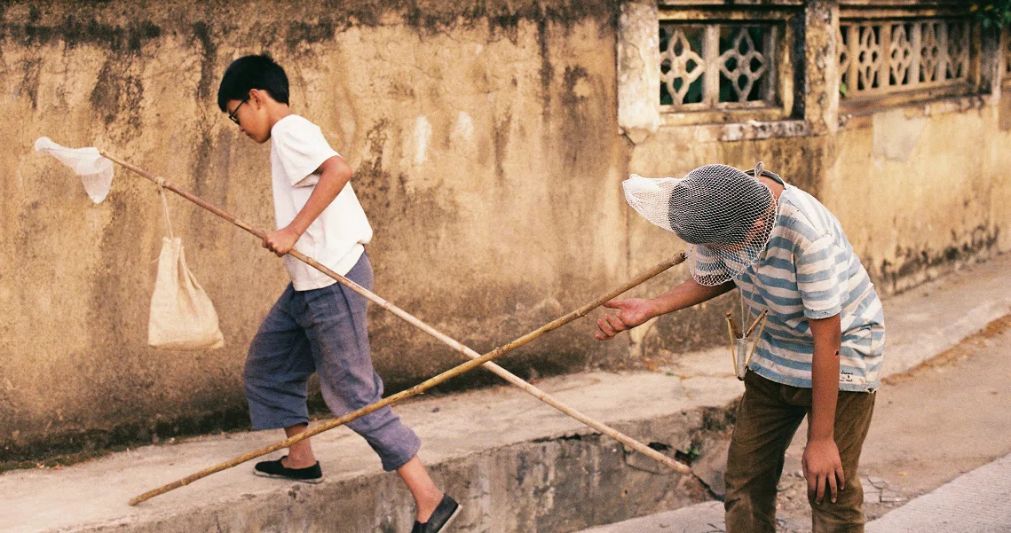 Film still from Changfeng Town showing two boys playing with sticks on a street, capturing everyday life in the movie.