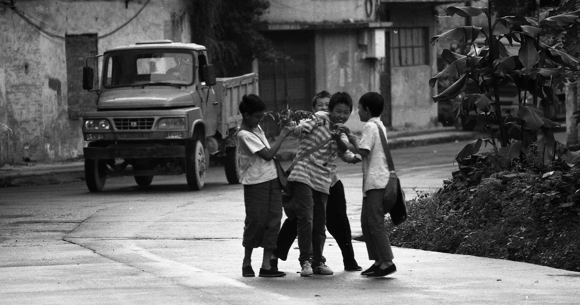 A black and white film still from Changfeng Town shows children playing in a street with a parked truck in the background.