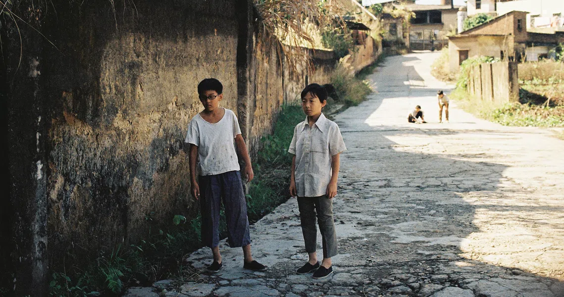 Two young boys stand on a dirt road in a rural village, a scene from the film Changfeng Town.