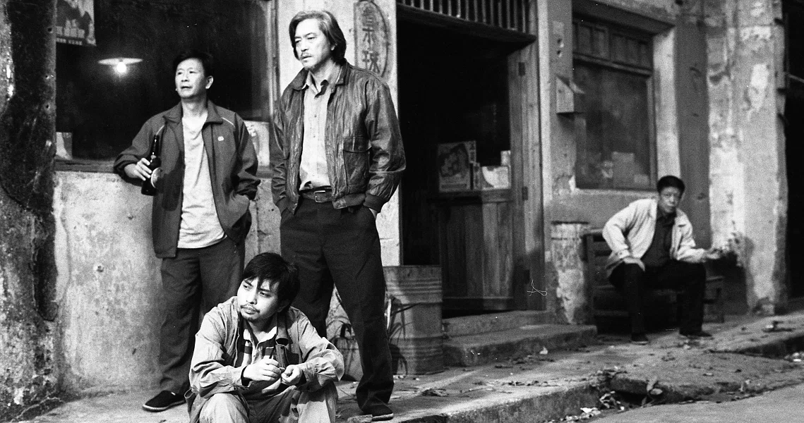 A black and white film still from Changfeng Town showing four men in various poses on a street, capturing the gritty urban atmosphere.