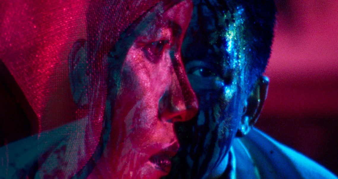 A close-up film still from "Demons" shows a character's face illuminated by vibrant pink and blue lighting, creating a dramatic atmosphere.