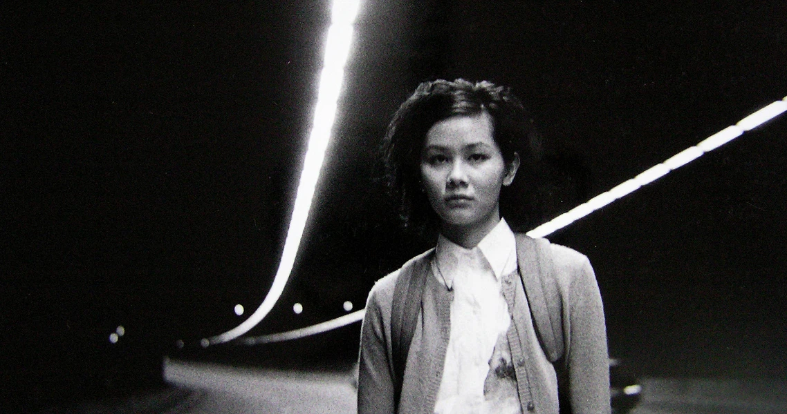 A black and white still from the film "Eating Air" shows a young person standing on a street at night with light trails visible.