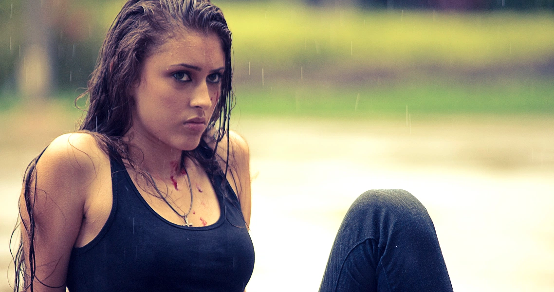 A young woman in a black tank top sits in the rain, looking intense in this dramatic still from the film Faeryville.