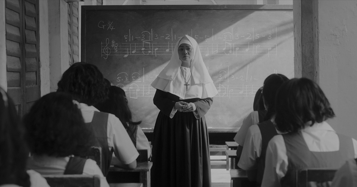 A nun teaches in a classroom from the film "From Victoria School To Ang Mo Kio", showing students and a chalkboard.