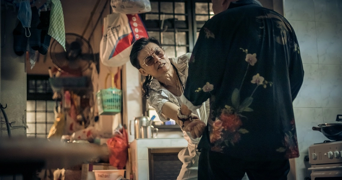 A tense scene from the film Geylang showing a person in a kitchen, with another figure looming in the foreground.