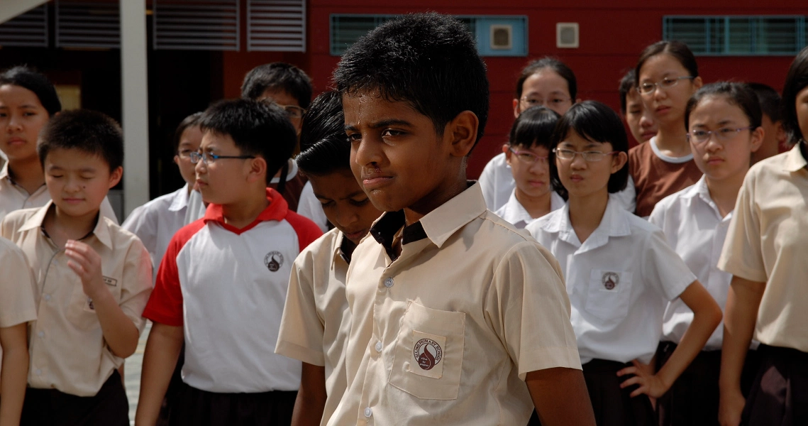 A scene from the film Gurushetram showing a group of diverse students in school uniforms, with a young boy in the foreground looking serious.