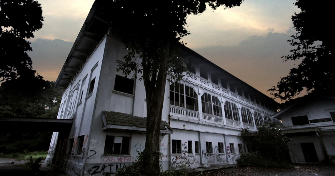 Film still from Haunted Changi showing an eerie abandoned building with graffiti at dusk, creating a spooky atmosphere.