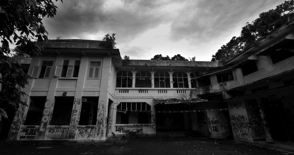 Eerie black and white still from "Haunted Changi" showing an abandoned colonial building with graffiti under a stormy sky.