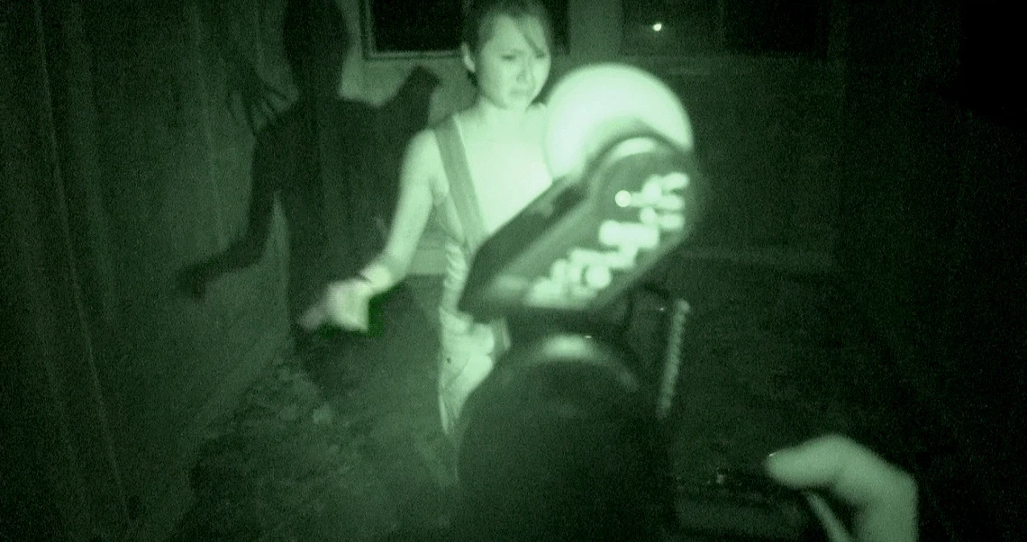 A night vision still from "Haunted Changi" shows a person holding a glowing device in a dark, eerie setting.