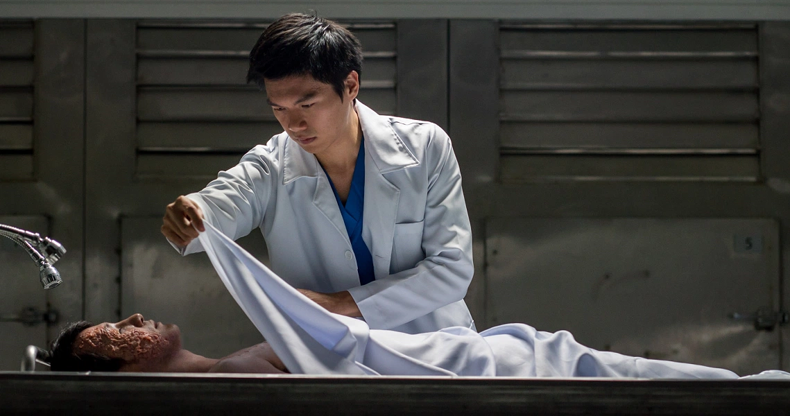 A doctor examines a covered body in a morgue scene from the film Hell Hole, depicting a tense moment in the thriller.