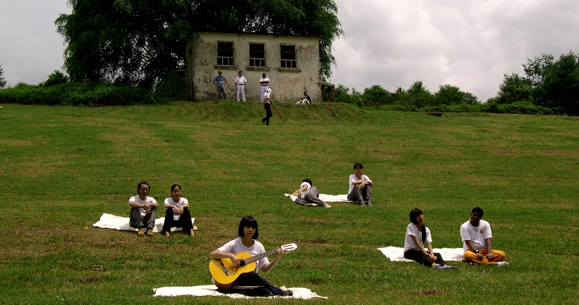 A scene from the film "Here" showing people relaxing on a grassy hill with an old house in the background.