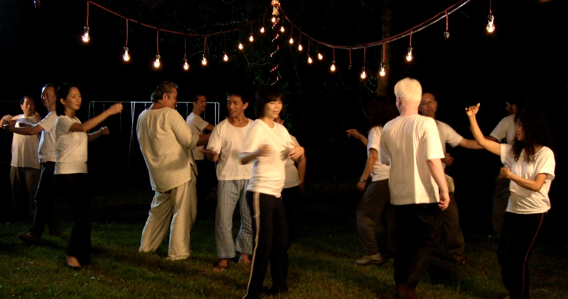 Group of people dancing outdoors at night under string lights in a scene from the film "Here".