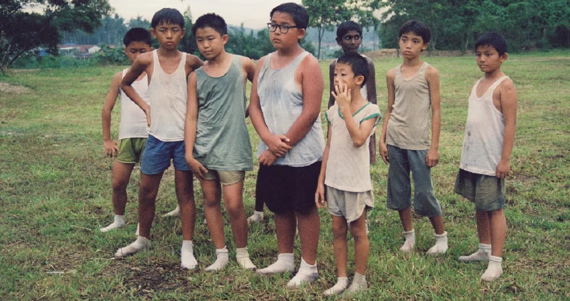 A group of young boys stand in a grassy field in a scene from the film Homerun, depicting rural childhood in Singapore.