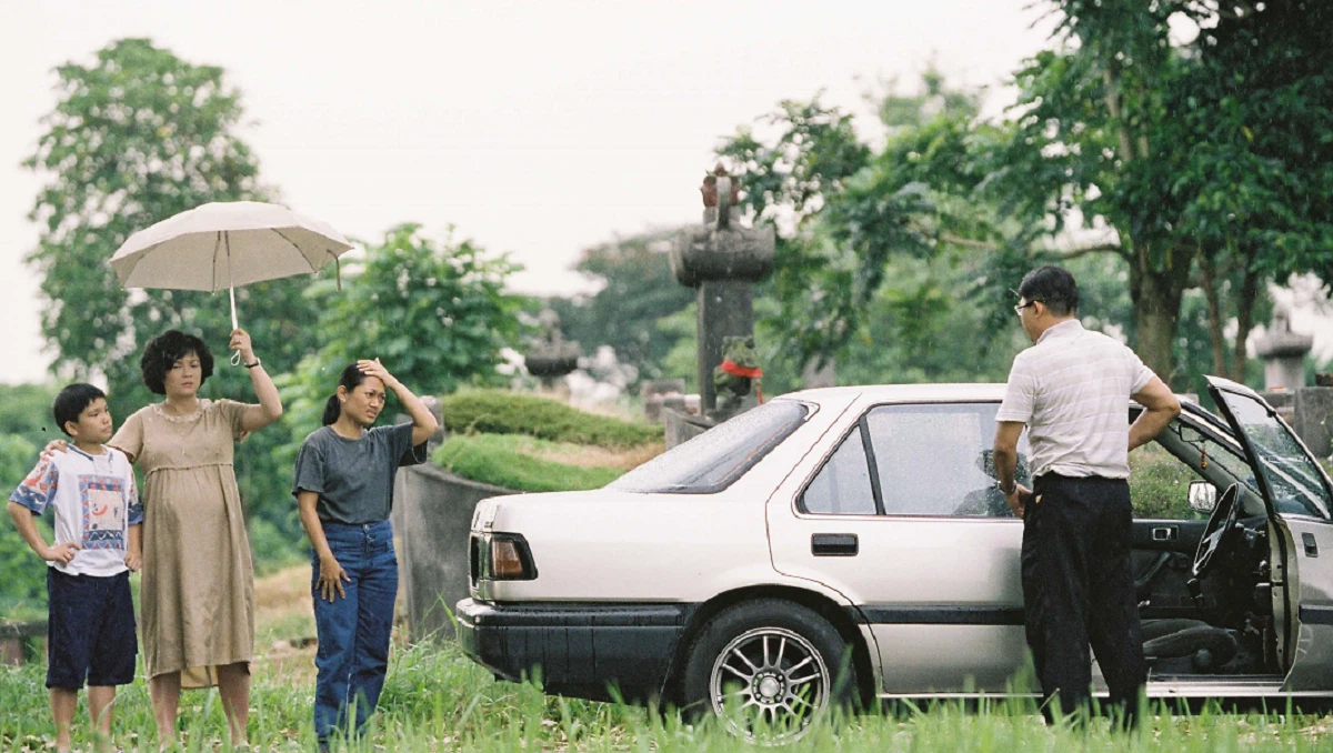 A family stands near a car in a rural setting, a scene from the Singaporean film Ilo Ilo.