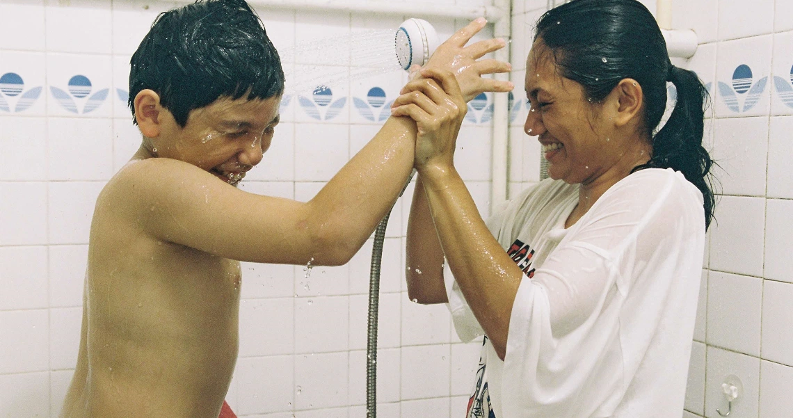 A scene from the film Ilo Ilo showing a woman helping a young boy shower, highlighting the caring relationship between characters.