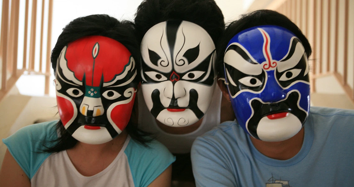 Three people wearing colorful Chinese opera masks in the film "In The House of Straw". Red, black, and blue designs on white backgrounds.