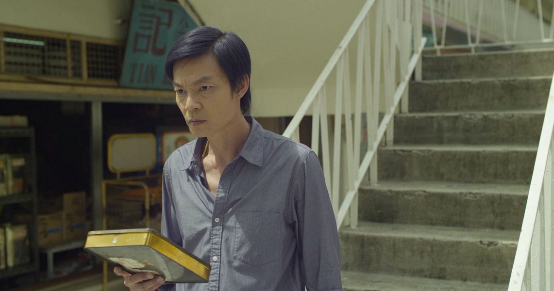 A scene from the film "Judgement Day" showing a young man holding a book while standing near a staircase in an interior setting.