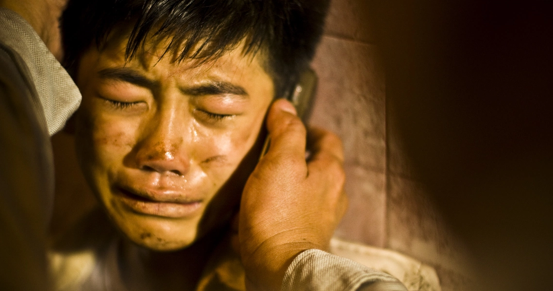 A tearful young boy from the film Kidnapper is comforted by an adult's hand on his cheek in this emotional scene.