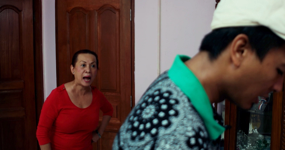 A scene from the film Konpaku showing a woman in a red top looking surprised as a man in traditional attire walks past.