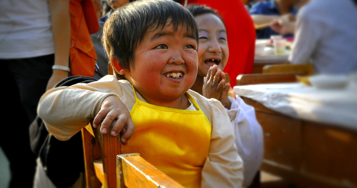 A joyful young boy in a yellow shirt laughs heartily in a scene from the film "Little People Big Dreams".