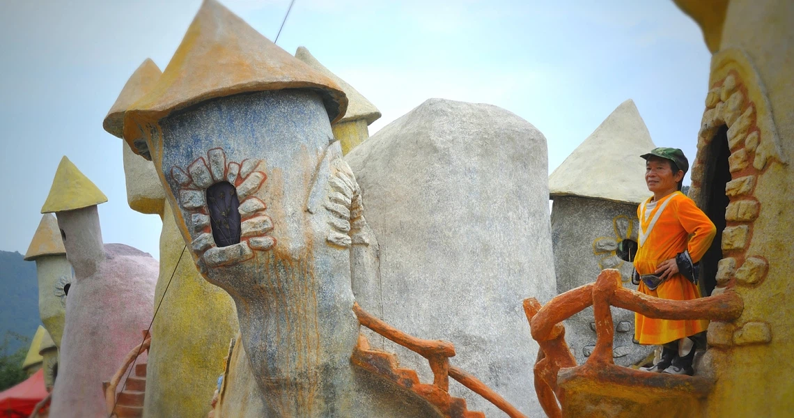 A film still from "Little People Big Dreams" showing a miniature figure sitting on a colorful, whimsical structure resembling a fantastical landscape.