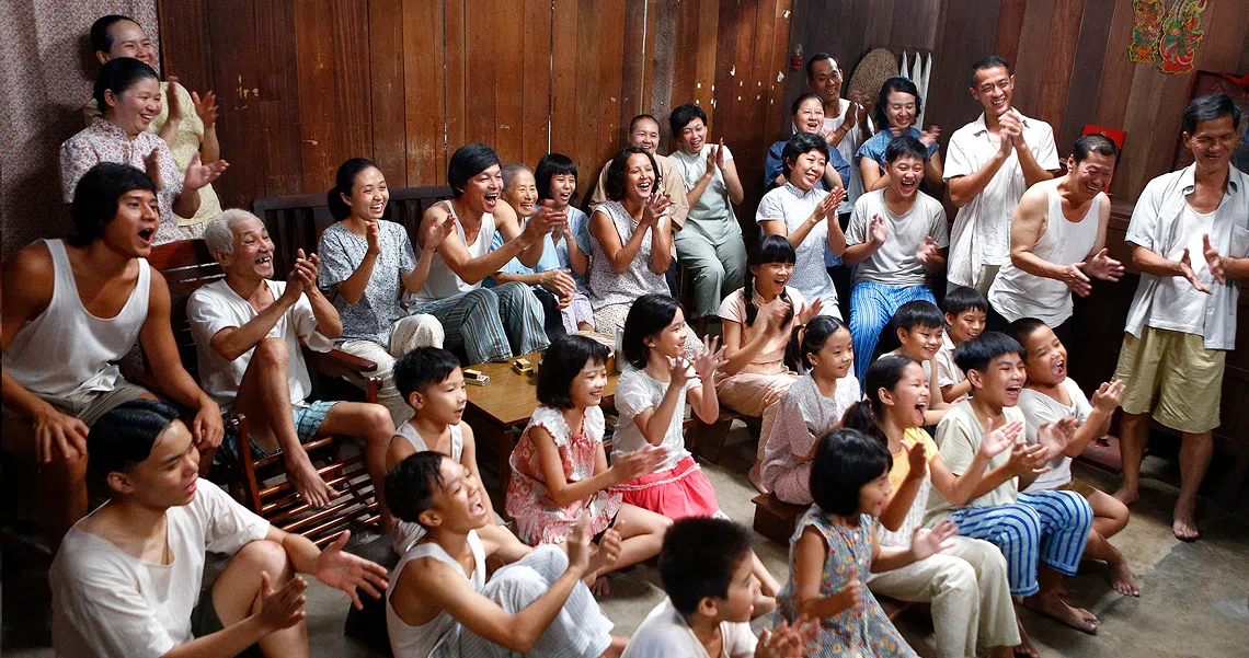 A large group of people in white shirts gather in a wooden-paneled room, depicting a scene from the film "A Long Long Time Ago".