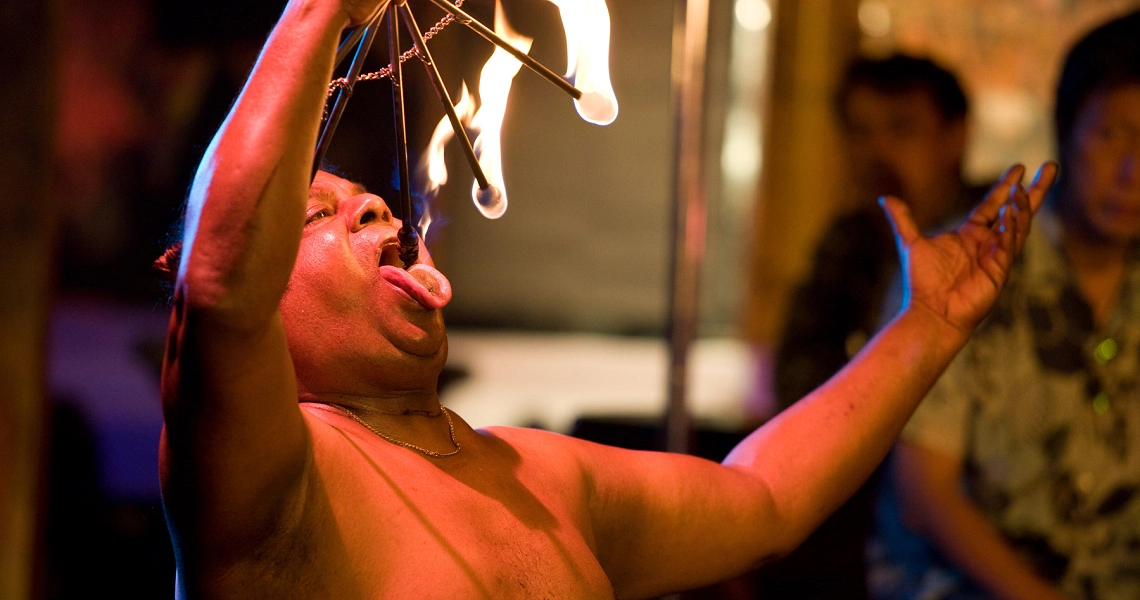 A dramatic scene from the film "My Magic" shows a shirtless man performing a fire-eating act, illuminated by blue and red lights.