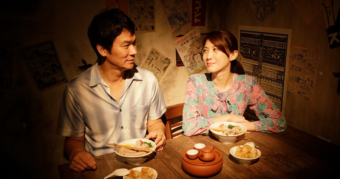 A scene from the film "Ramen Teh" showing two characters dining together in a dimly lit room with various dishes on the table.