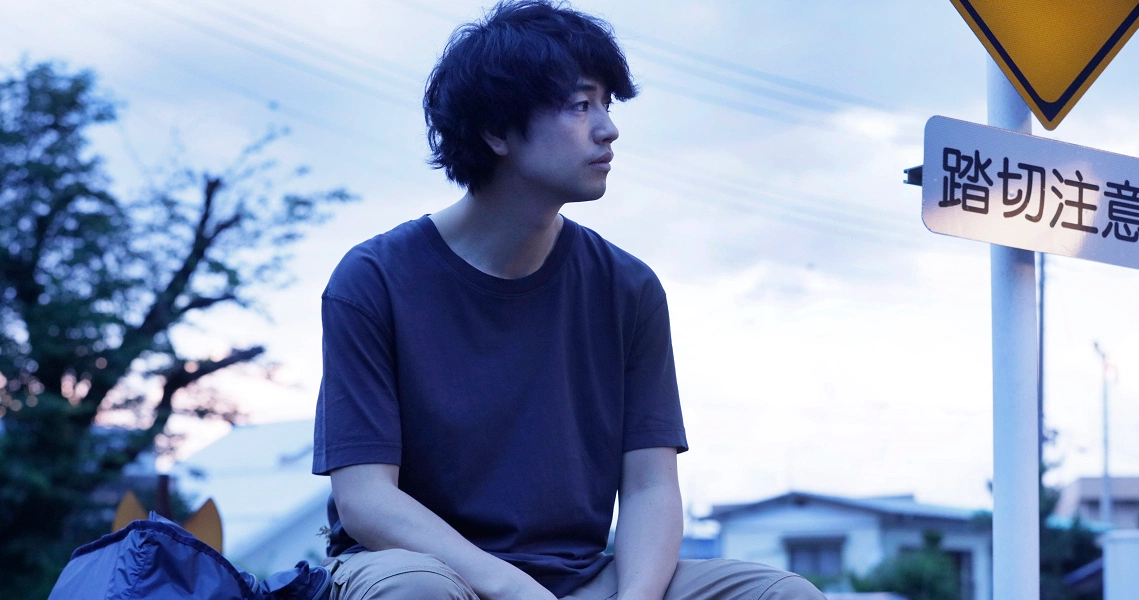 A young man in a blue shirt sits pensively by a road sign in a scene from the film "Ramen Teh".