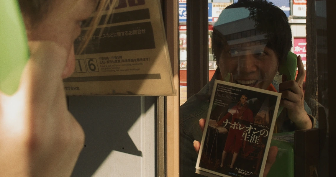 A person peers through a window, holding a sign in the film Revolution Launderette. Neon lights reflect in the background.