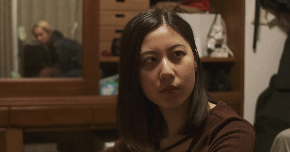 A scene from Revolution Launderette shows a woman with long dark hair in a laundromat, looking pensive. Another person is visible in the background.