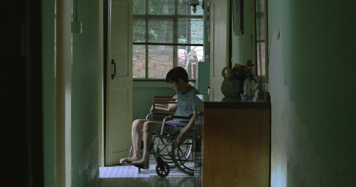 A scene from the Singaporean film 'Sandcastle' showing a young man sitting in a dimly lit room, looking pensive.