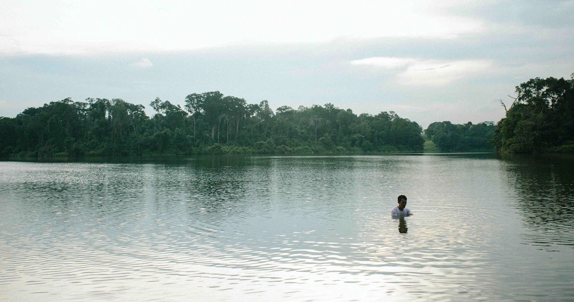 A woman stands waist-deep in still water, reflecting on her surroundings in a scene from the film 'Standing in Still Water'.